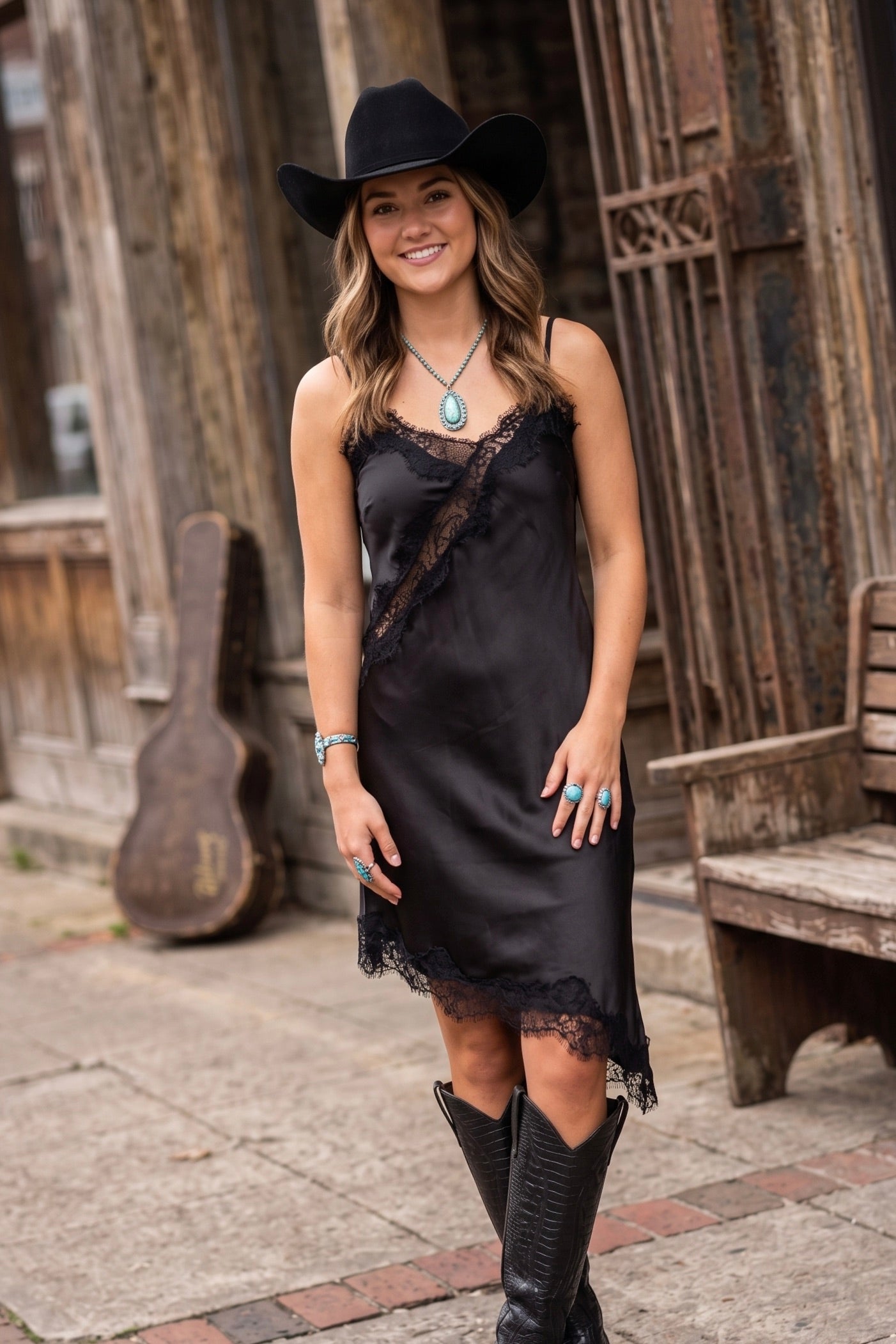 Women's black satin slip cami dress featuring floral lace trim, adjustable spaghetti straps, and a relaxed midi silhouette.