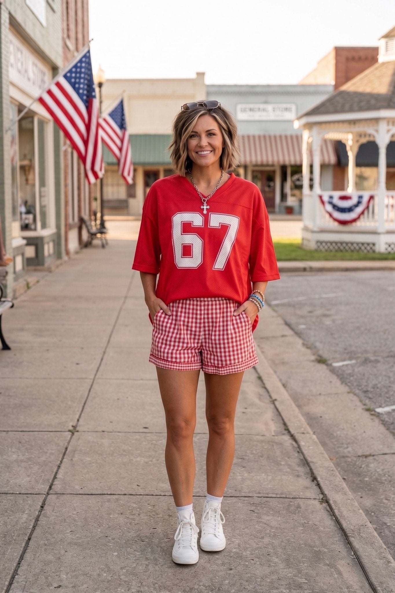 Red oversized Americana football jersey paired with red gingham shorts and white sneakers, styled as a casual Fourth of July outfit perfect for summer celebrations, country concerts, and patriotic weekend wear.