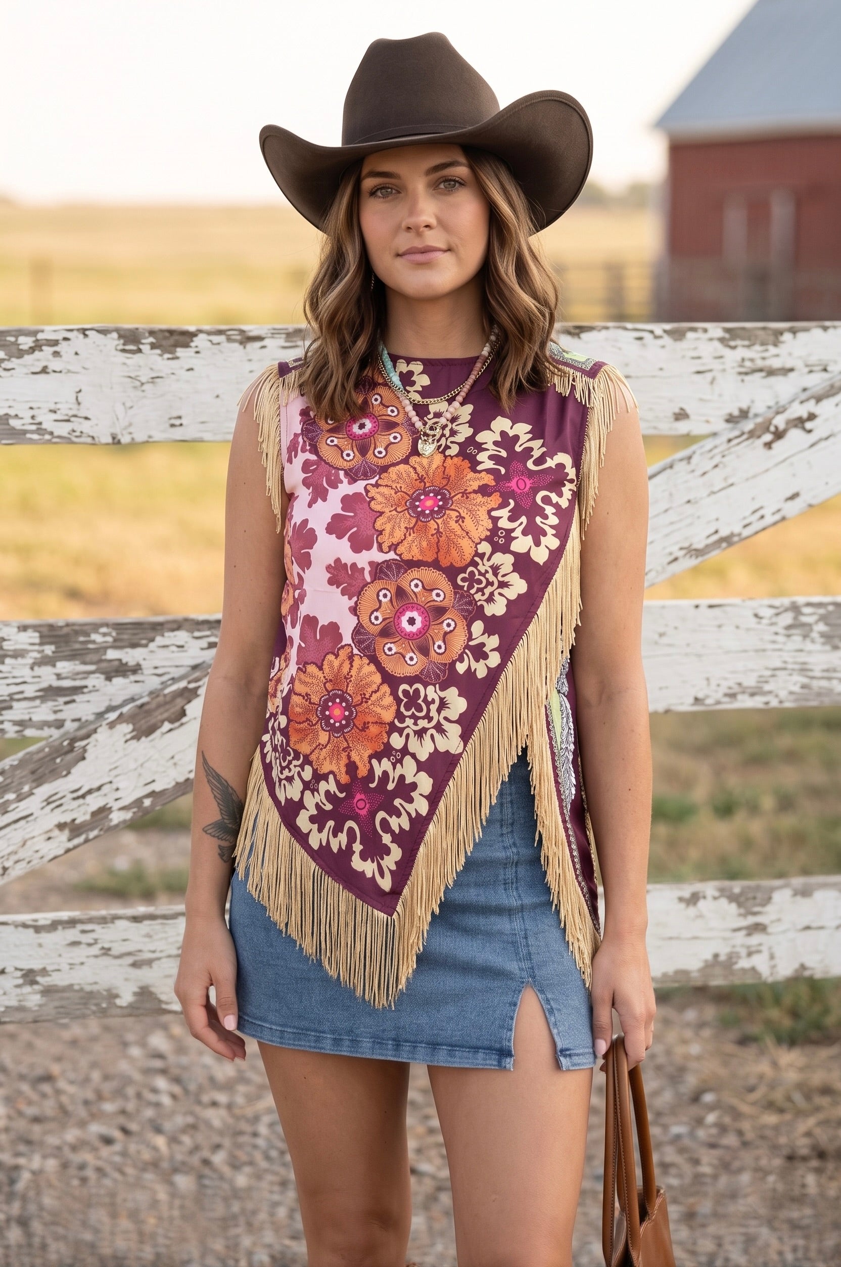 Women's floral patchwork fringe top with asymmetrical hem and V-neckline in burgundy and pink tones styled with a denim skirt and cowboy hat.