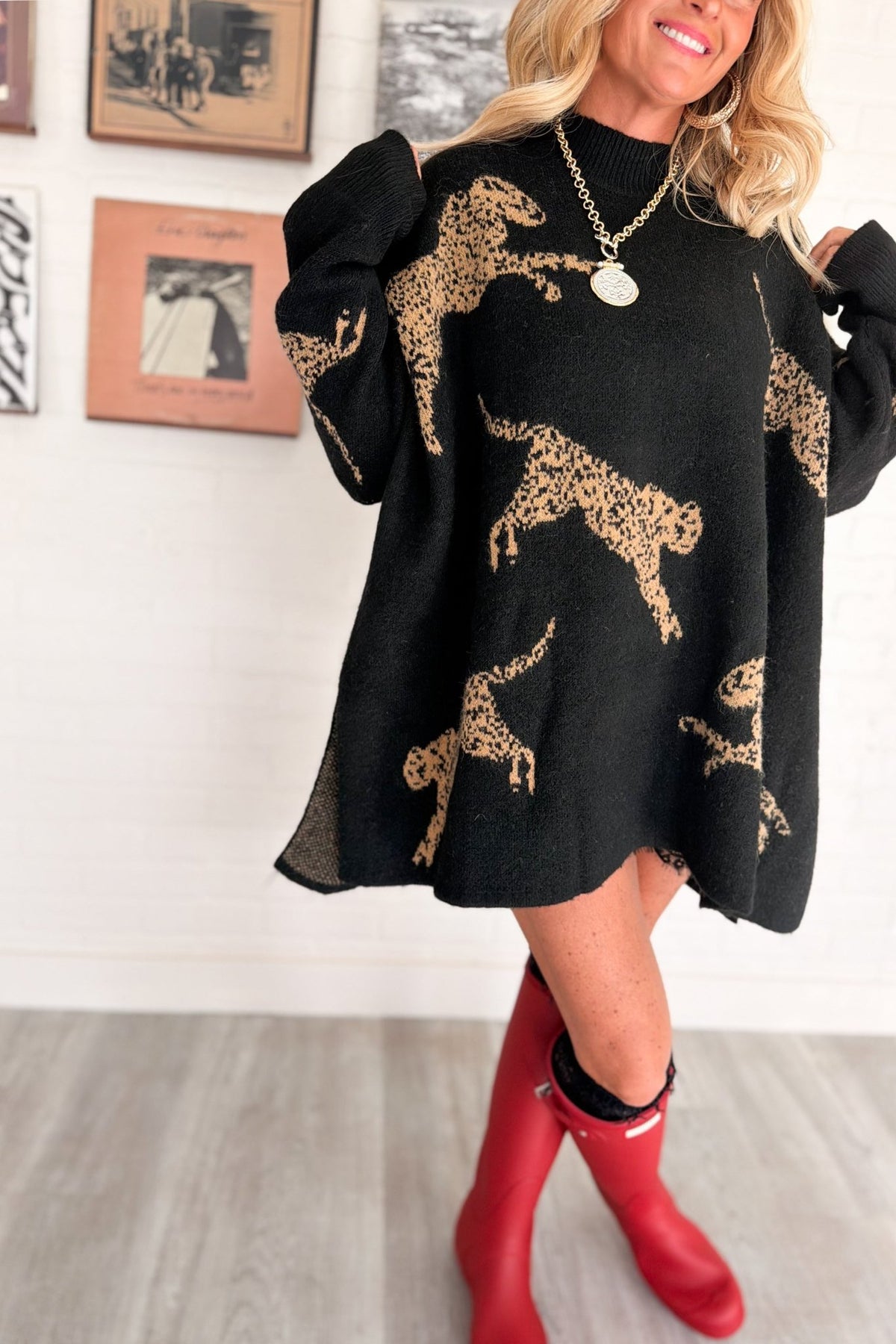 Women’s oversized black knit mock neck sweater featuring large camel cheetah animal motifs throughout, dropped shoulders, relaxed long sleeves, ribbed cuffs, and an extra-long tunic silhouette.