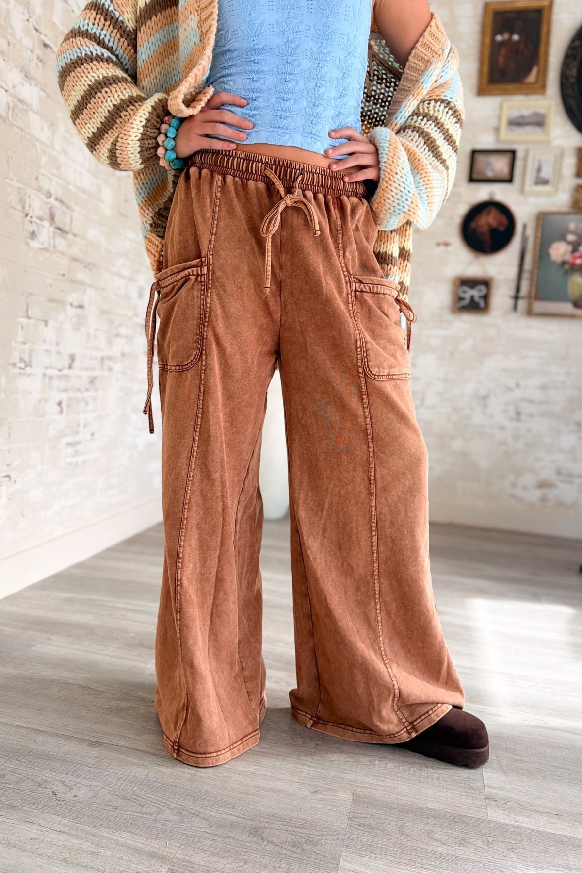 Women’s rust brown washed wide leg pants featuring a relaxed fit, elastic drawstring waistband, oversized front patch pockets, contrast seam detailing and a soft lived-in finish. Casual pull-on pants with a loose straight wide leg silhouette for boho, casual, lounge and everyday outfits.