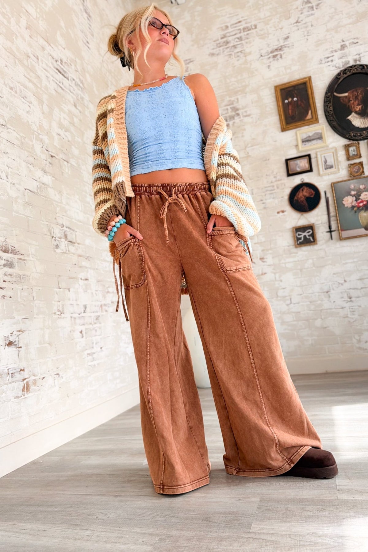Women’s rust brown washed wide leg pants featuring a relaxed fit, elastic drawstring waistband, oversized front patch pockets, contrast seam detailing and a soft lived-in finish. Casual pull-on pants with a loose straight wide leg silhouette for boho, casual, lounge and everyday outfits.