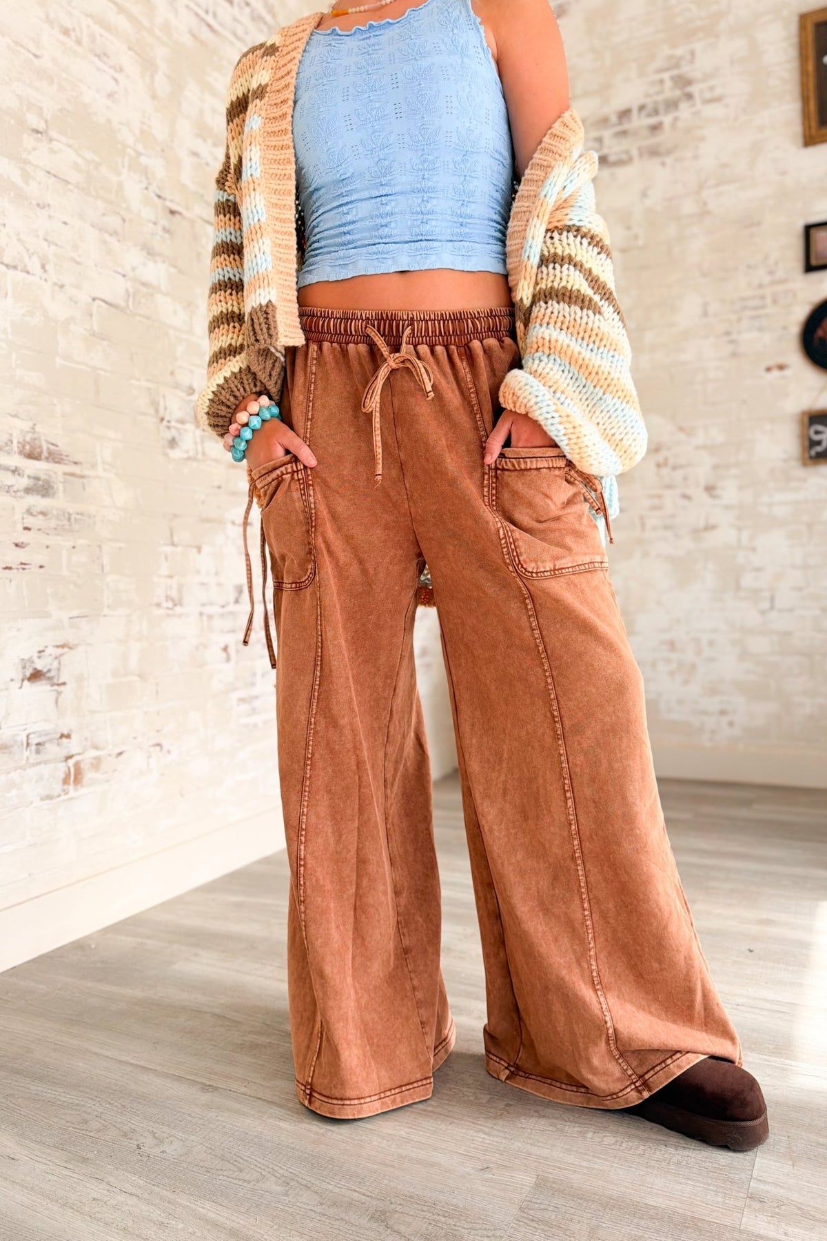Women’s rust brown washed wide leg pants featuring a relaxed fit, elastic drawstring waistband, oversized front patch pockets, contrast seam detailing and a soft lived-in finish. Casual pull-on pants with a loose straight wide leg silhouette for boho, casual, lounge and everyday outfits.
