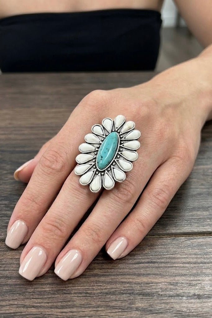 Oversized Navajo-inspired adjustable statement ring featuring a natural turquoise center stone, white floral accents, and an antique silver finish with an adjustable dual brass band.