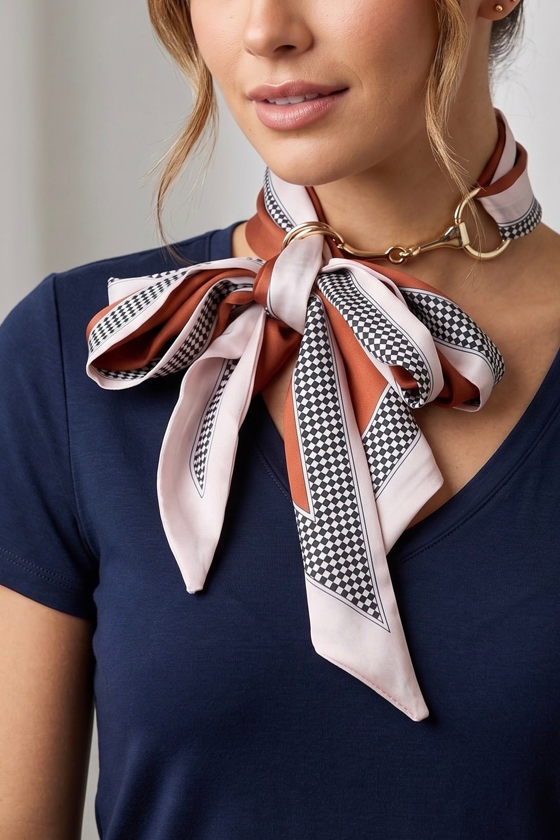 Silky red and blush pink checker print scarf necklace featuring polished gold horsebit hardware styled as a chic equestrian-inspired neck accessory.