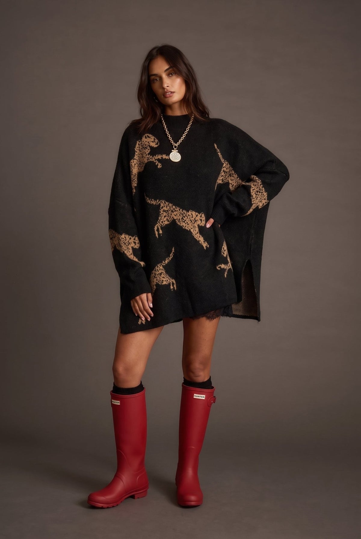 Women’s oversized black knit mock neck sweater featuring large camel cheetah animal motifs throughout, dropped shoulders, relaxed long sleeves, ribbed cuffs, and an extra-long tunic silhouette.
