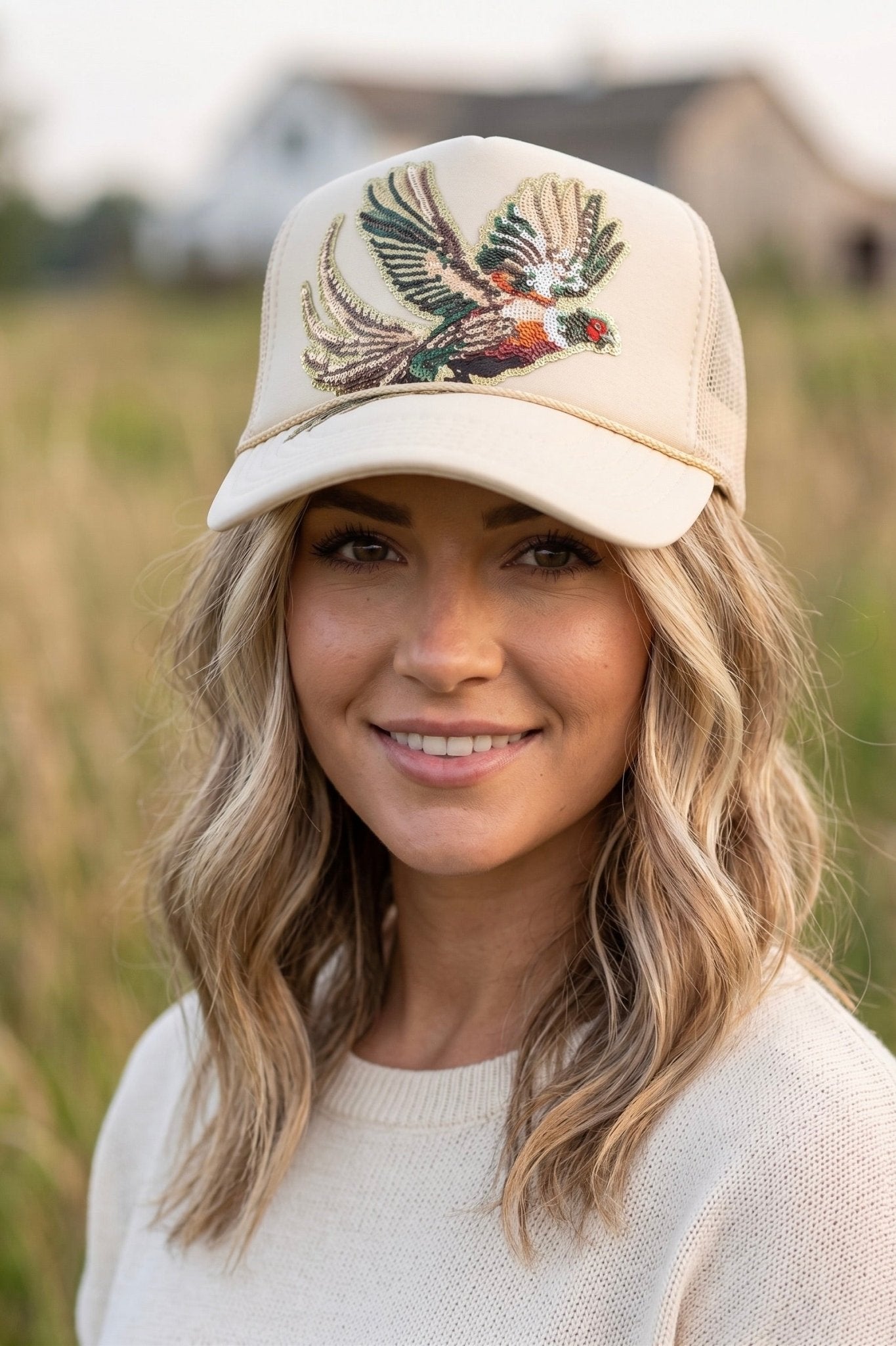 Cream premium foam trucker hat featuring a large multicolor sequin pheasant patch, breathable mesh back, and adjustable snapback closure.