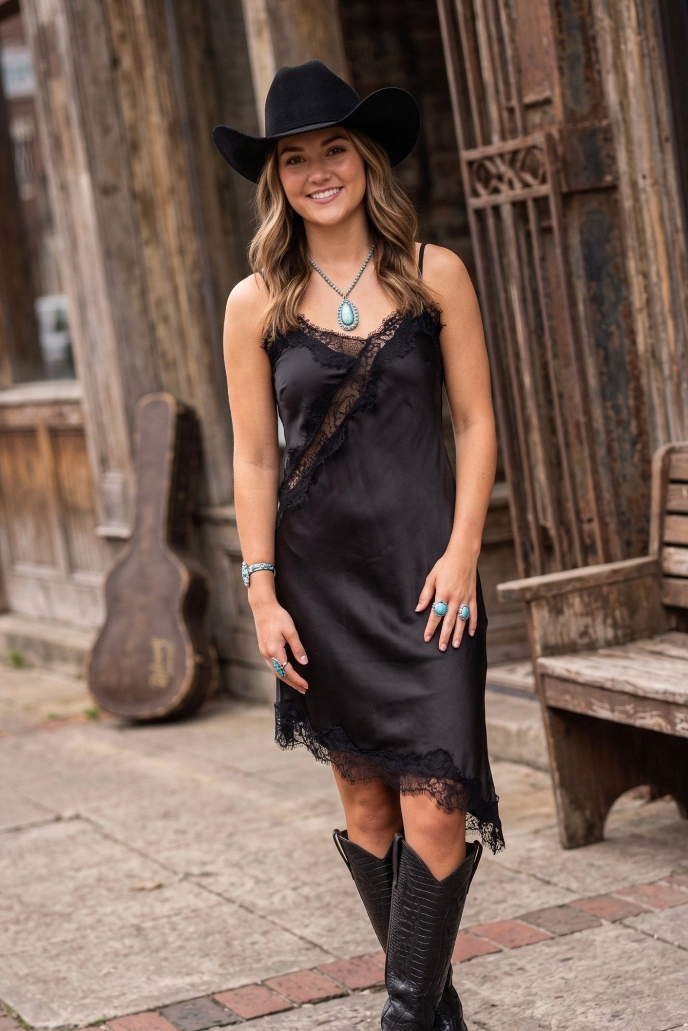 Women's black satin slip cami dress featuring floral lace trim, adjustable spaghetti straps, and a relaxed midi silhouette.