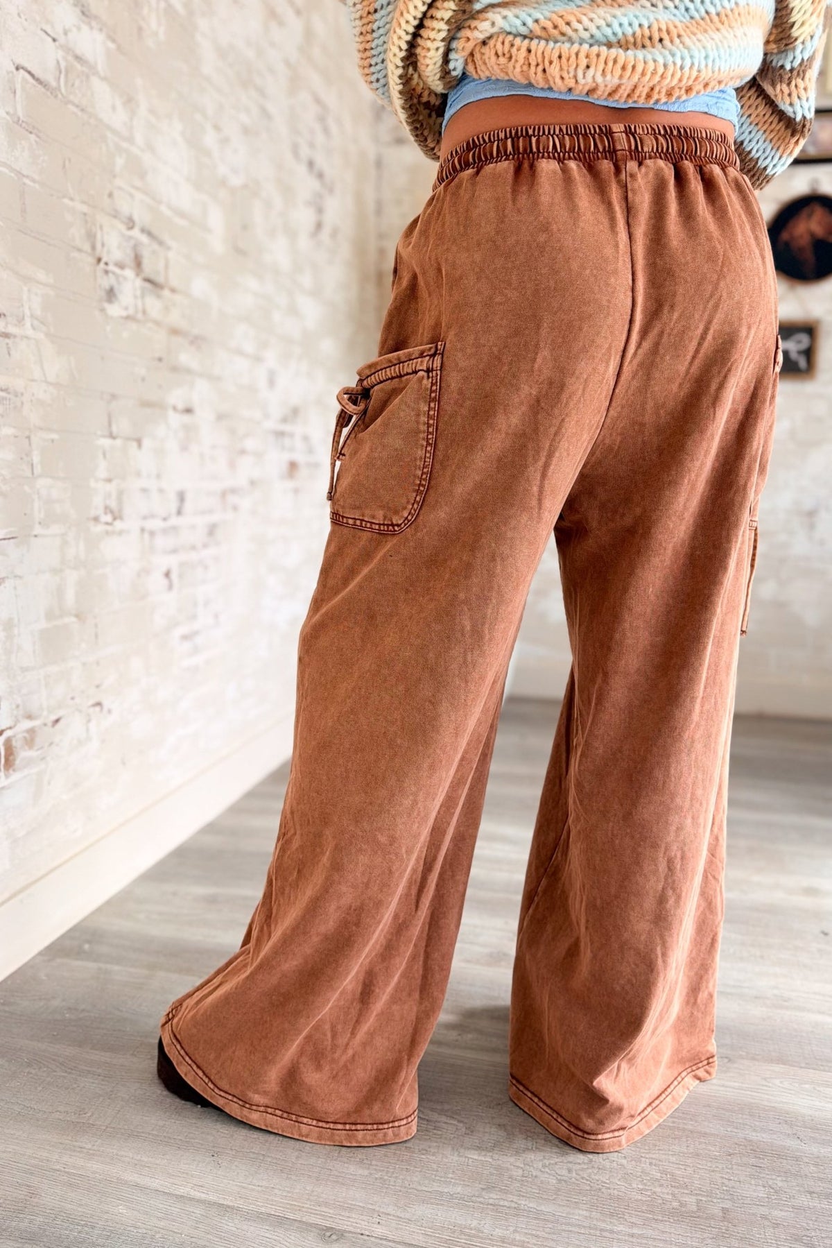 Women’s rust brown washed wide leg pants featuring a relaxed fit, elastic drawstring waistband, oversized front patch pockets, contrast seam detailing and a soft lived-in finish. Casual pull-on pants with a loose straight wide leg silhouette for boho, casual, lounge and everyday outfits.
