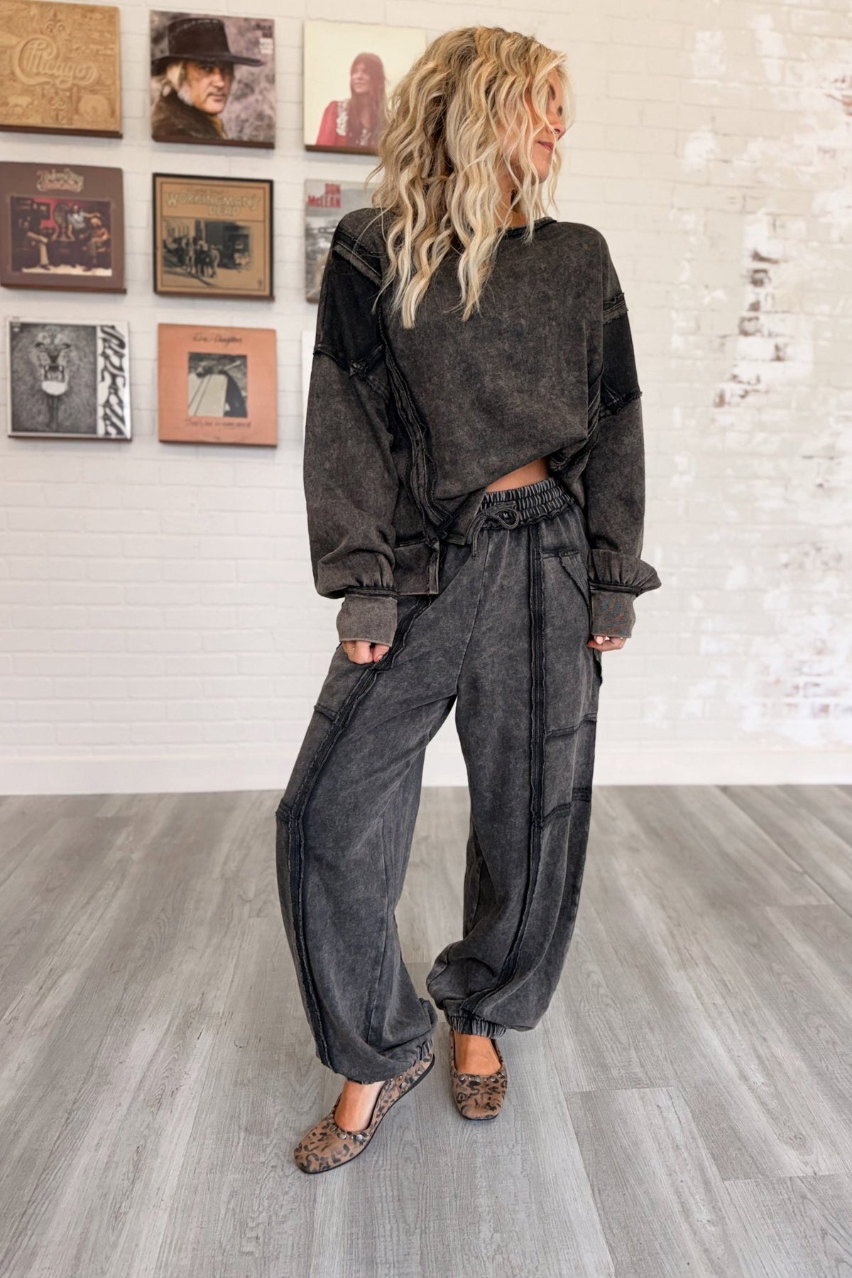 Women’s washed black mineral-washed two-piece lounge set featuring an oversized slightly cropped crewneck sweatshirt with exposed seam detailing and matching relaxed balloon jogger pants with an elastic drawstring waist, oversized patch pockets, exposed seams, and gathered ankles.