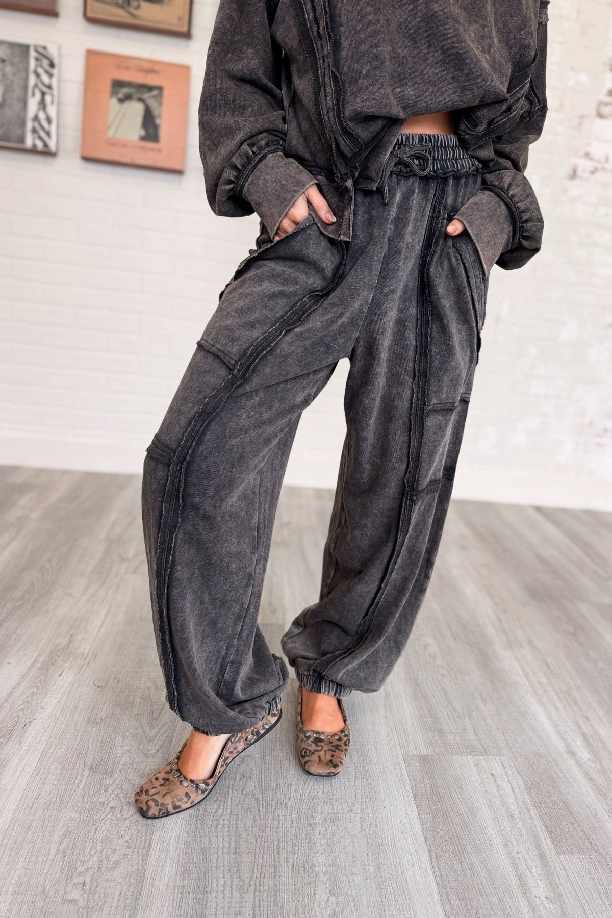 Women’s washed black mineral-washed two-piece lounge set featuring an oversized slightly cropped crewneck sweatshirt with exposed seam detailing and matching relaxed balloon jogger pants with an elastic drawstring waist, oversized patch pockets, exposed seams, and gathered ankles.
