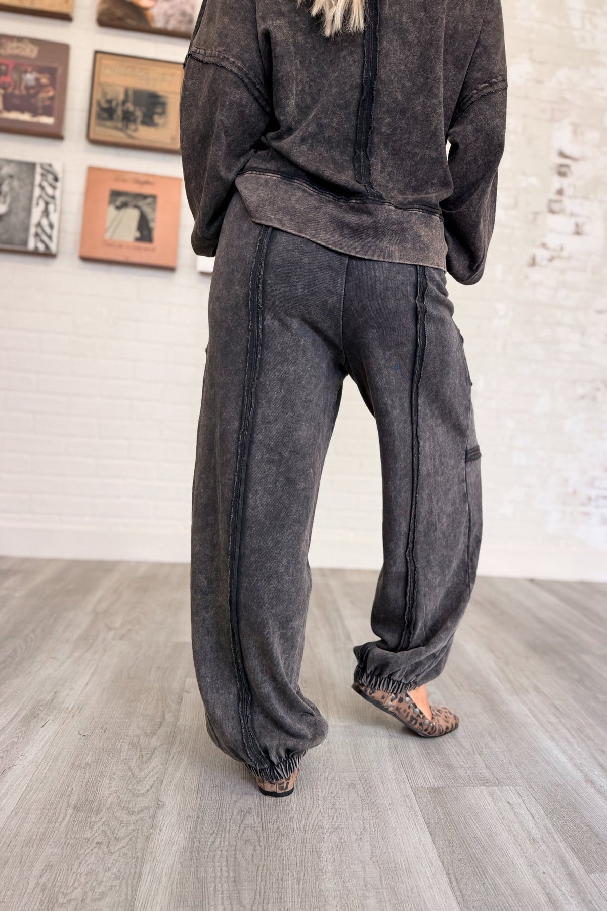 Women’s washed black mineral-washed two-piece lounge set featuring an oversized slightly cropped crewneck sweatshirt with exposed seam detailing and matching relaxed balloon jogger pants with an elastic drawstring waist, oversized patch pockets, exposed seams, and gathered ankles.