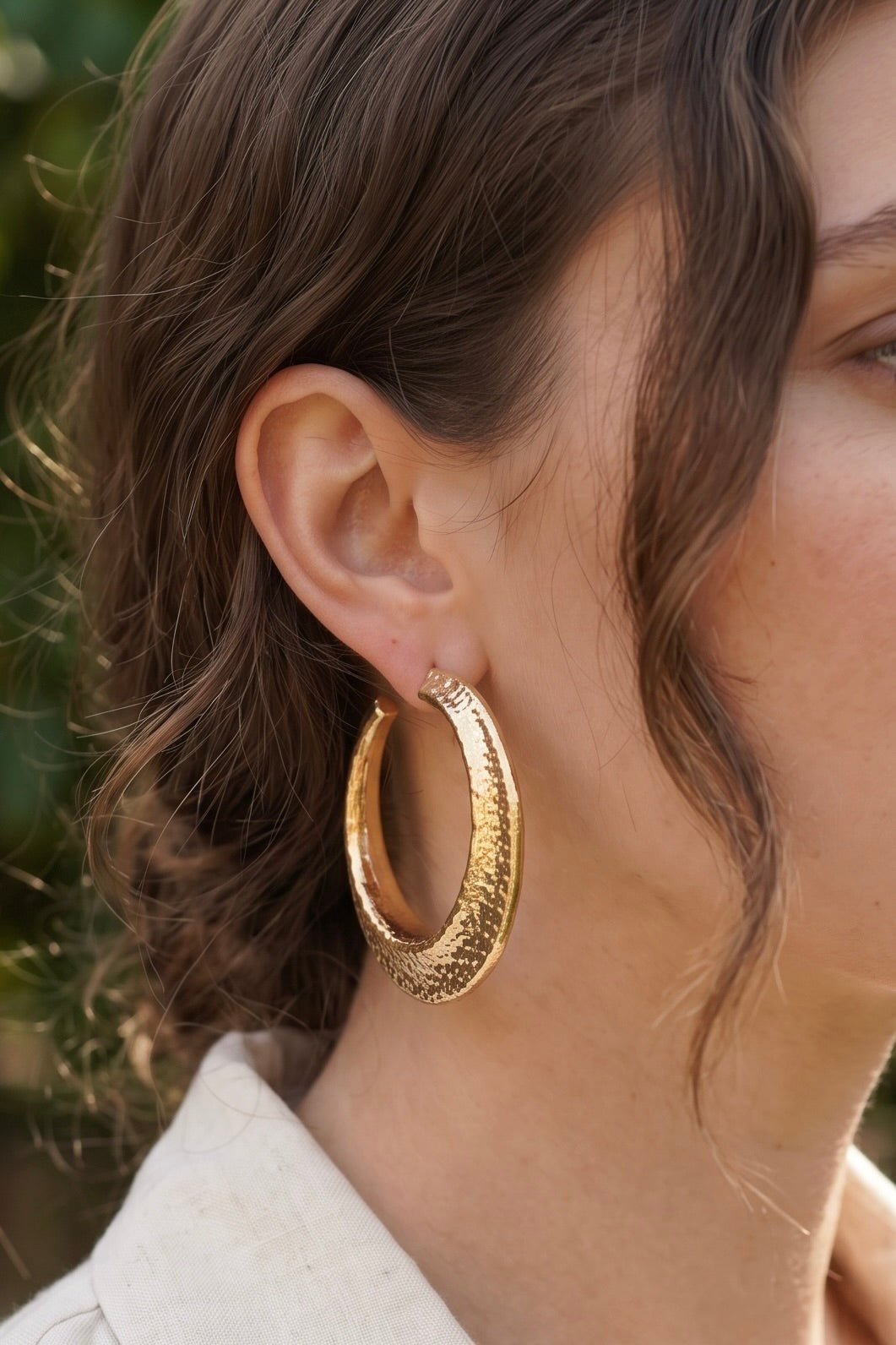 Women’s worn gold statement hoop earrings featuring a bold sculptural crescent shape, hammered textured surface, gold dipped finish, and hypoallergenic post backs.