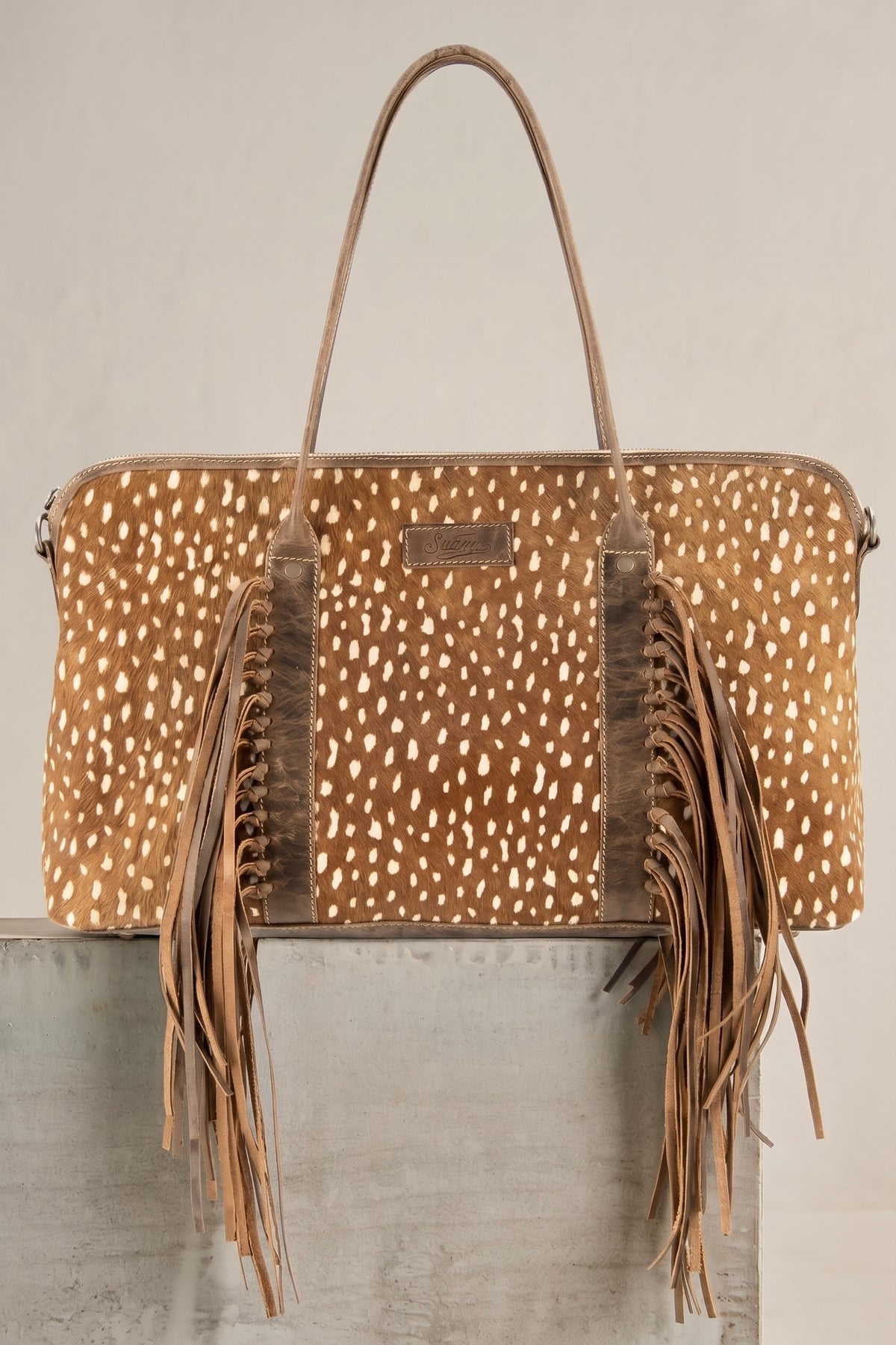 Oversized genuine spotted cowhide and full grain leather Western bag with long brown leather fringe and double shoulder handles.