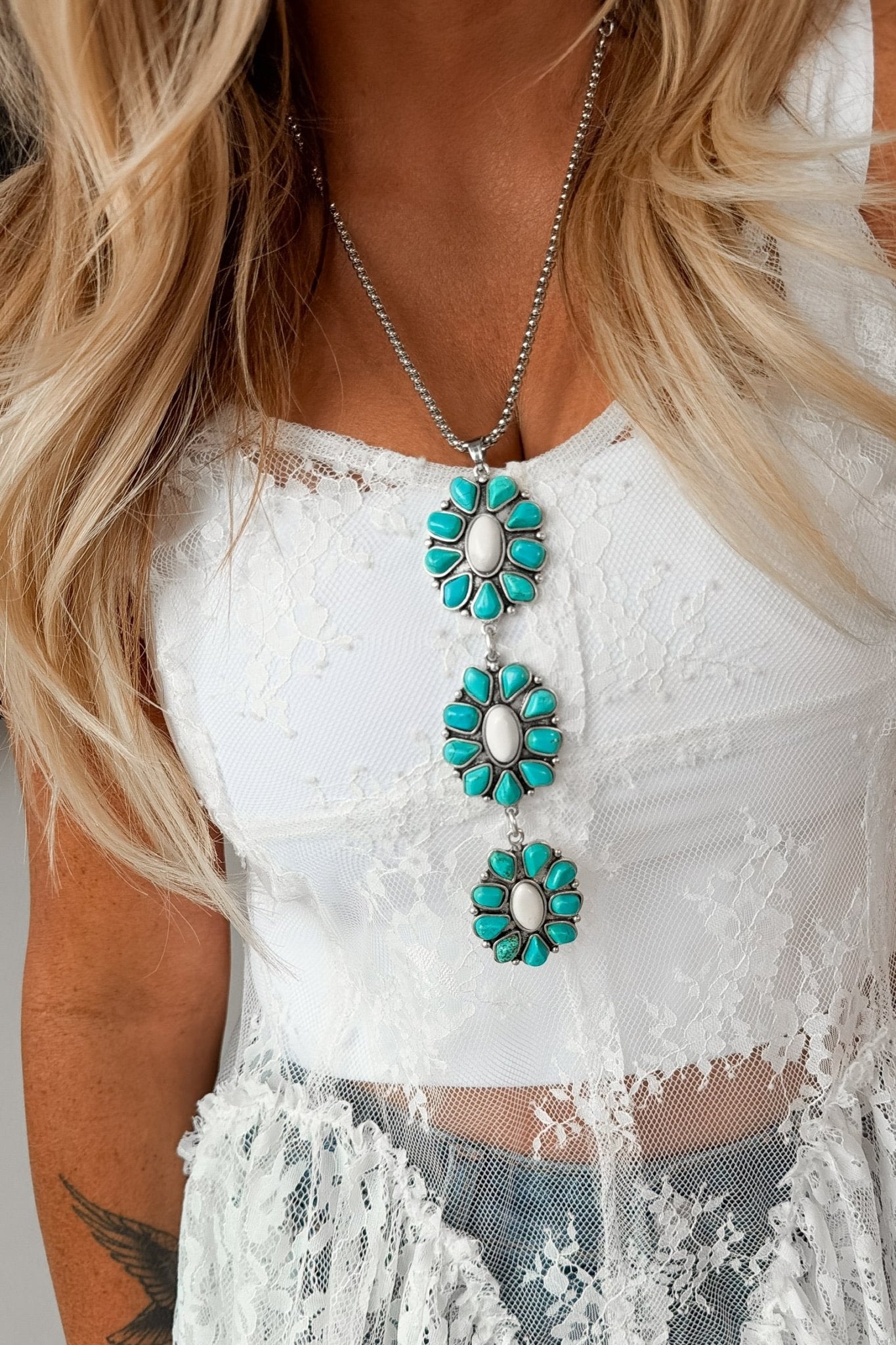Long western necklace featuring turquoise and ivory floral-inspired pendants with antique silver detailing, styled with a lace top for a classic Southwestern look.