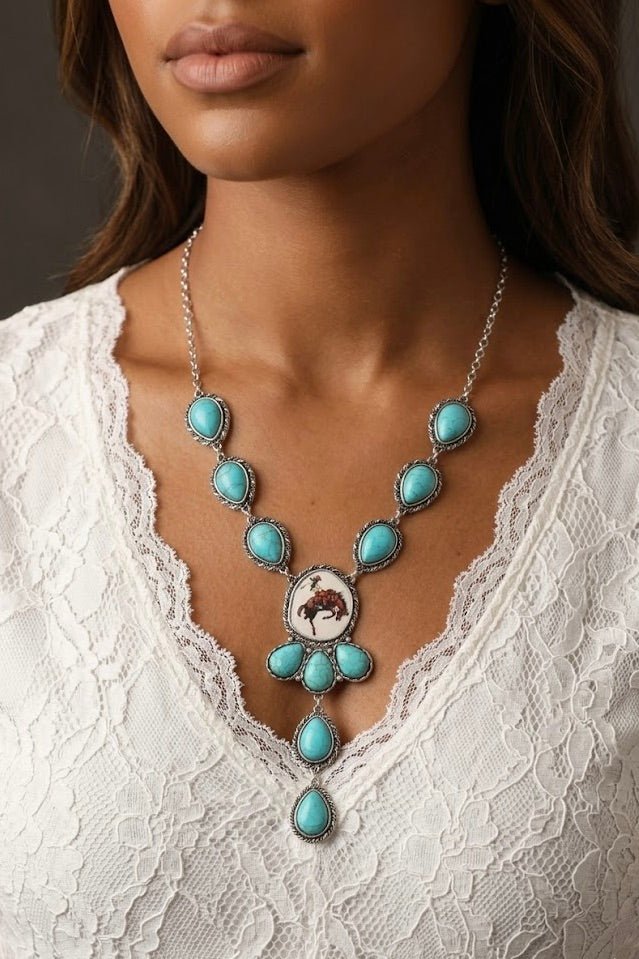 Silver statement necklace featuring multiple teardrop turquoise stones along the chain and drop, centered with a round pendant of a bronc rider