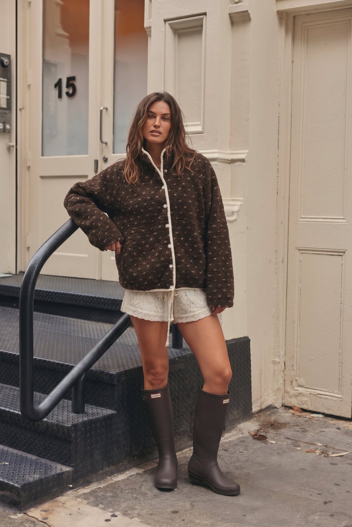 Women's chocolate brown sherpa fleece jacket featuring an ultra-plush, fuzzy teddy bear texture with an allover scattered ivory speckled dot pattern. Designed with a cozy high mock neckline, contrasting cream trim along the front opening and collar, white snap-button front closure, relaxed oversized silhouette, dropped shoulders,  This soft, textured sherpa jacket features a slightly cropped, boxy fit with a rounded hem, combining vintage-inspired
