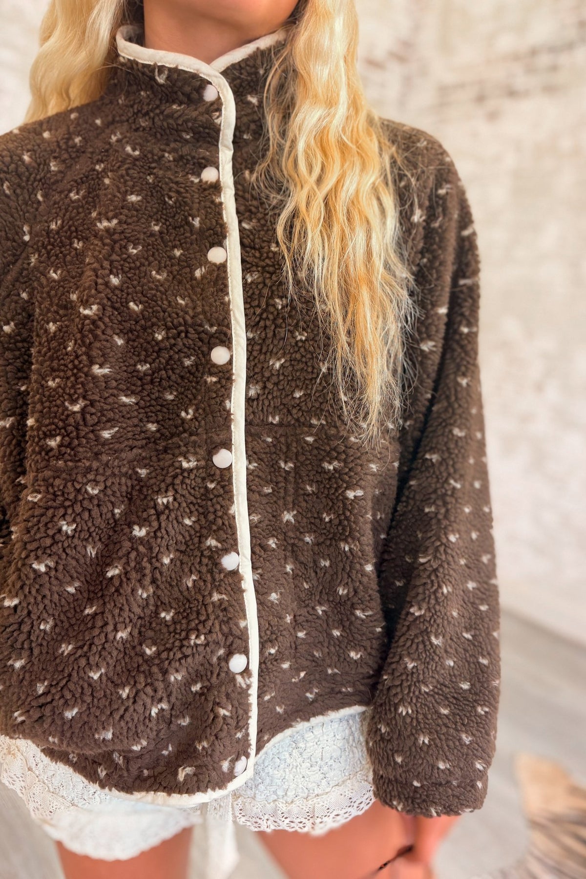 Women's chocolate brown sherpa fleece jacket featuring an ultra-plush, fuzzy teddy bear texture with an allover scattered ivory speckled dot pattern. Designed with a cozy high mock neckline, contrasting cream trim along the front opening and collar, white snap-button front closure, relaxed oversized silhouette, dropped shoulders,  This soft, textured sherpa jacket features a slightly cropped, boxy fit with a rounded hem, combining vintage-inspired